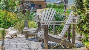 A wooden deck with Adirondack chairs, surrounded by a garden with rocks and plants. - Counting Pelicans + Ocean View + Pelican Hunt (Kill Devil Hills)