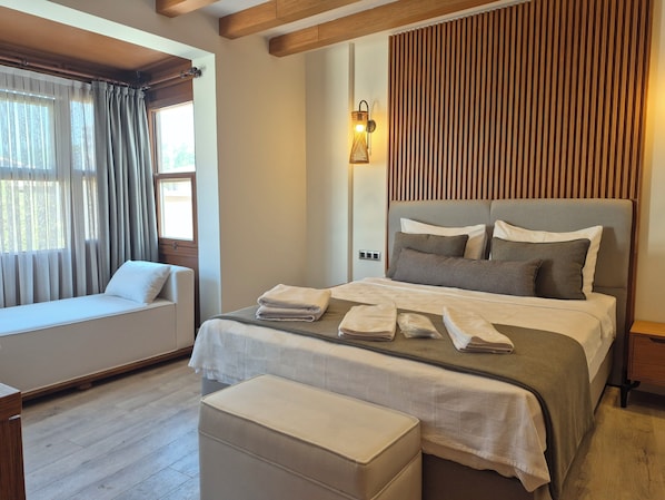 Un dormitorio bien iluminado con cama, mesitas de noche, ventana con cortinas y techo de madera.
