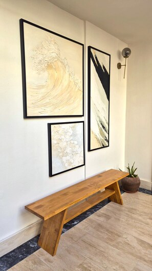 A hallway with three framed abstract paintings on the wall, a wooden bench, and a potted plant. - EDRA HOUSE  (Cesme)