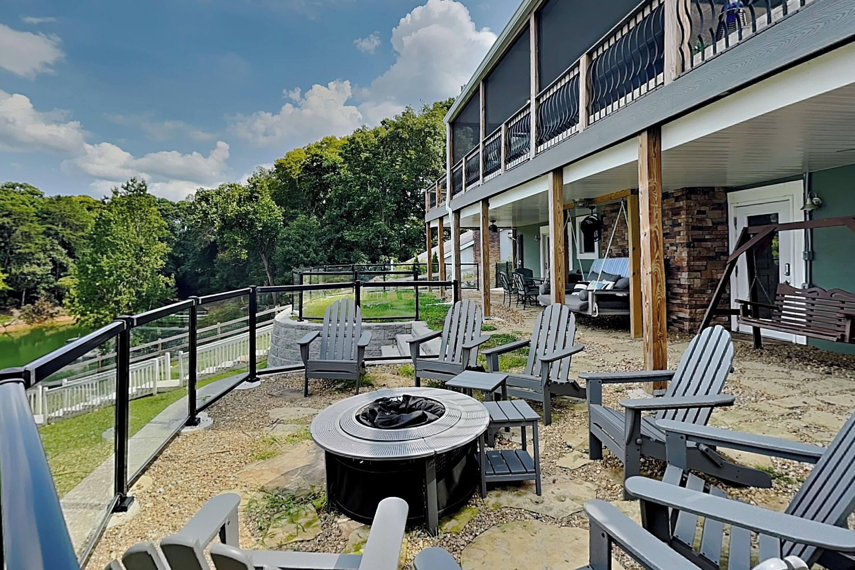 Un patio exterior con sillas Adirondack, un brasero y vistas a un lago.