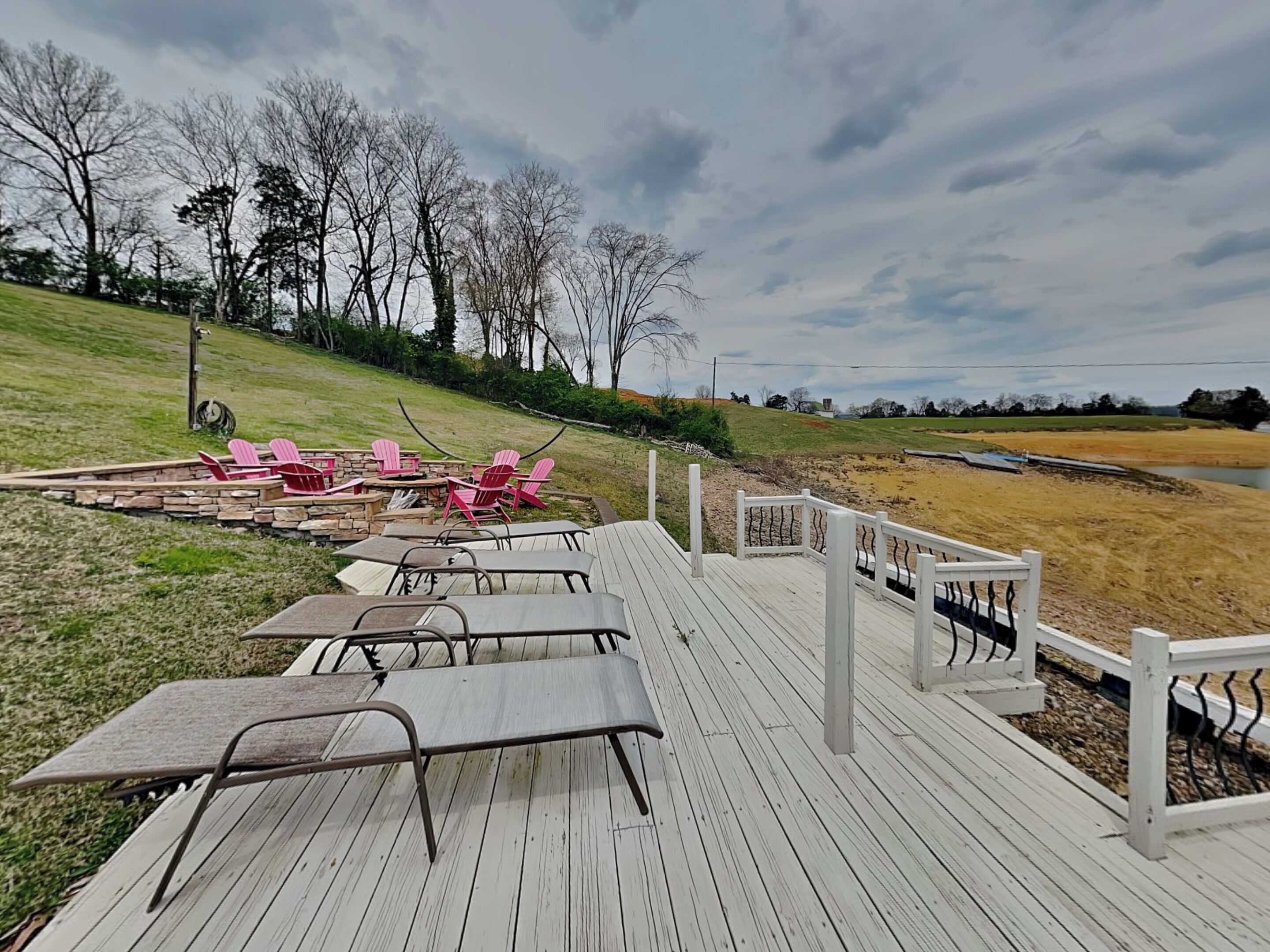 A wooden deck with metal chairs and tables, overlooking a grassy area and a body of water.