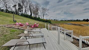 A wooden deck with metal chairs and tables, overlooking a grassy area and a body of water.