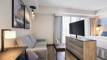 Habitación de hotel con cama, escritorio, silla, televisión y obras de arte en las paredes.