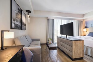 Habitación de hotel con cama, escritorio, silla, televisión y obras de arte en las paredes.