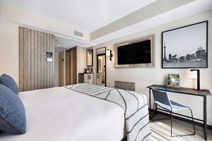 Hotelkamer met een groot bed, een bureau, een stoel, een televisie en een stadsbeeld aan de muur.