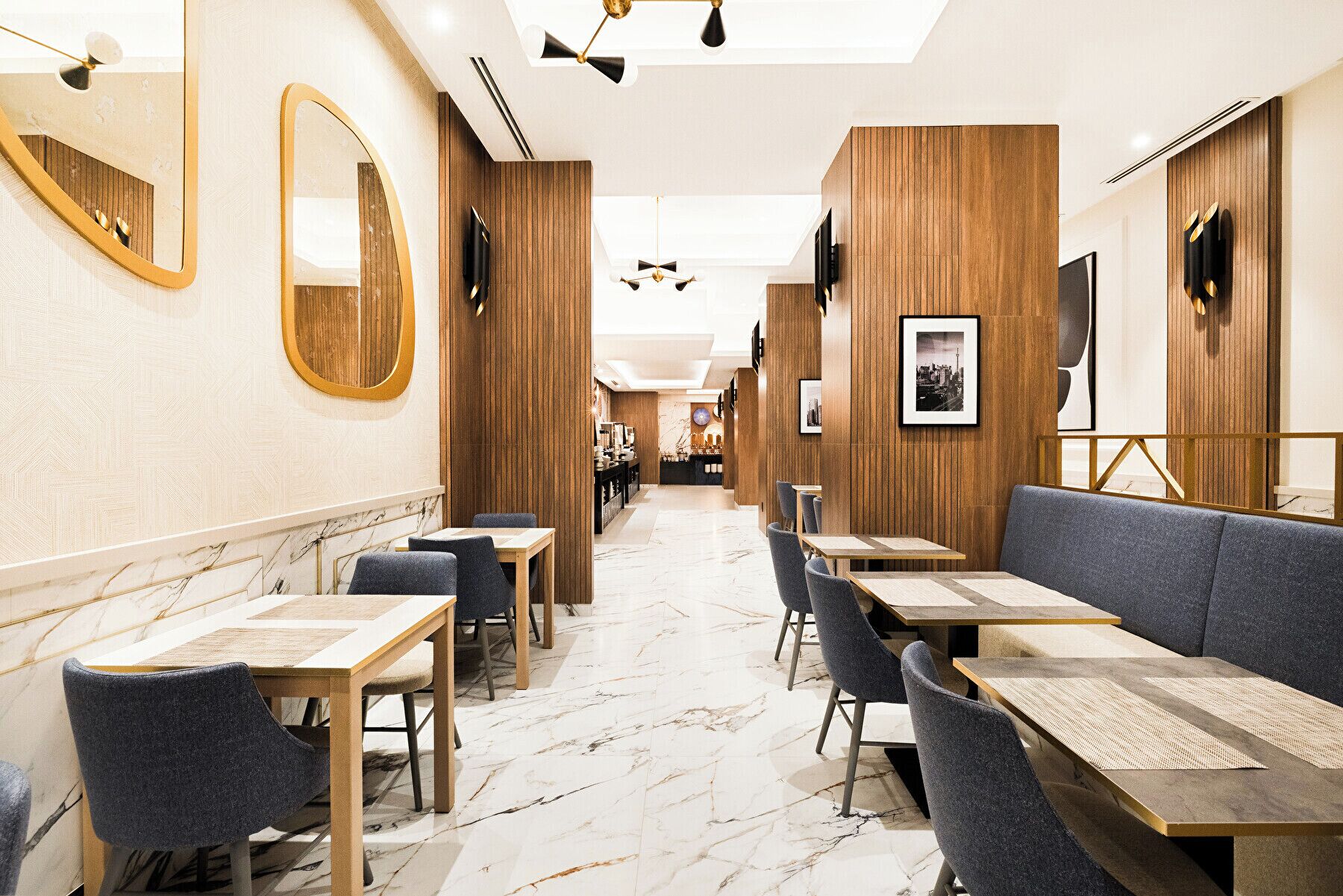 A modern restaurant interior with marble flooring, wooden panel walls, and a mix of table and booth seating.