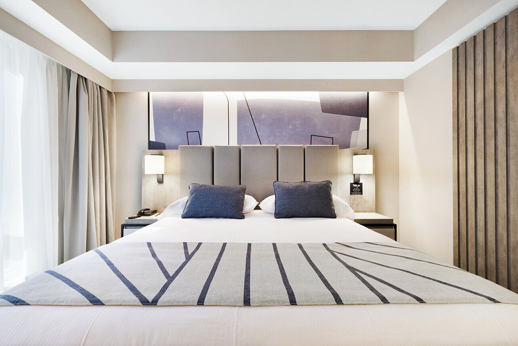 Een moderne hotelkamer met een groot bed, twee bedlampen en een hoofdeinde met een geometrisch ontwerp.