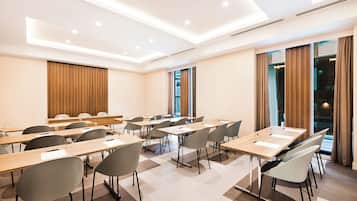 Een moderne congreszaal met meerdere tafels en stoelen, grote ramen met gordijnen en inbouwverlichting.