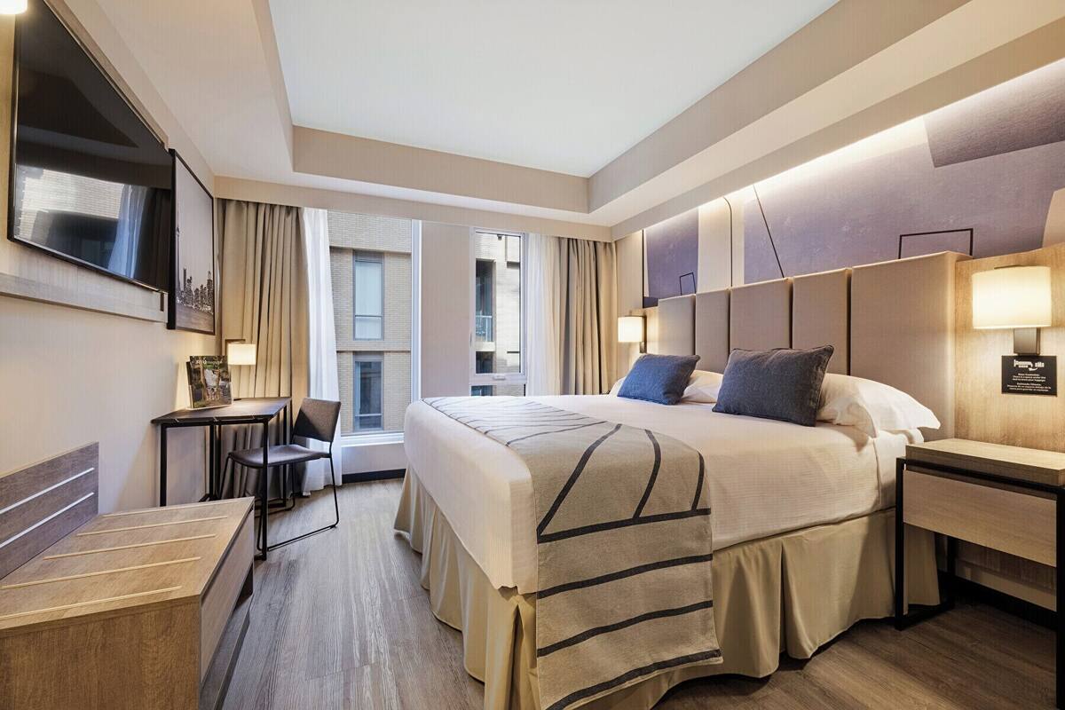 A modern hotel room with a large bed, bedside tables, a desk, and a TV mounted on the wall.