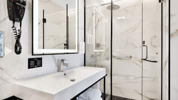A modern bathroom with a white sink, a hairdryer, a glass-enclosed shower, and marble walls.