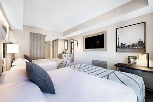 Een hotelkamer met twee bedden, een bureau, een televisie en een stadsgezichtschilderij.