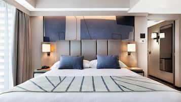 Una habitación de hotel moderna con una cama grande, dos lámparas de noche, un cabecero con motivos geométricos y vistas a la ciudad por la ventana.