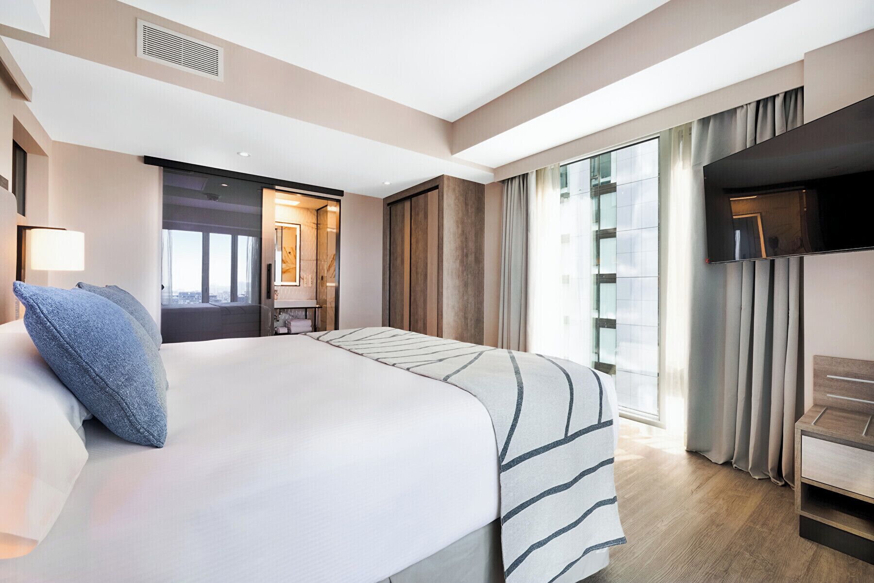 Una habitación de hotel moderna con una cama grande, un escritorio, un televisor y una ventana con cortinas.