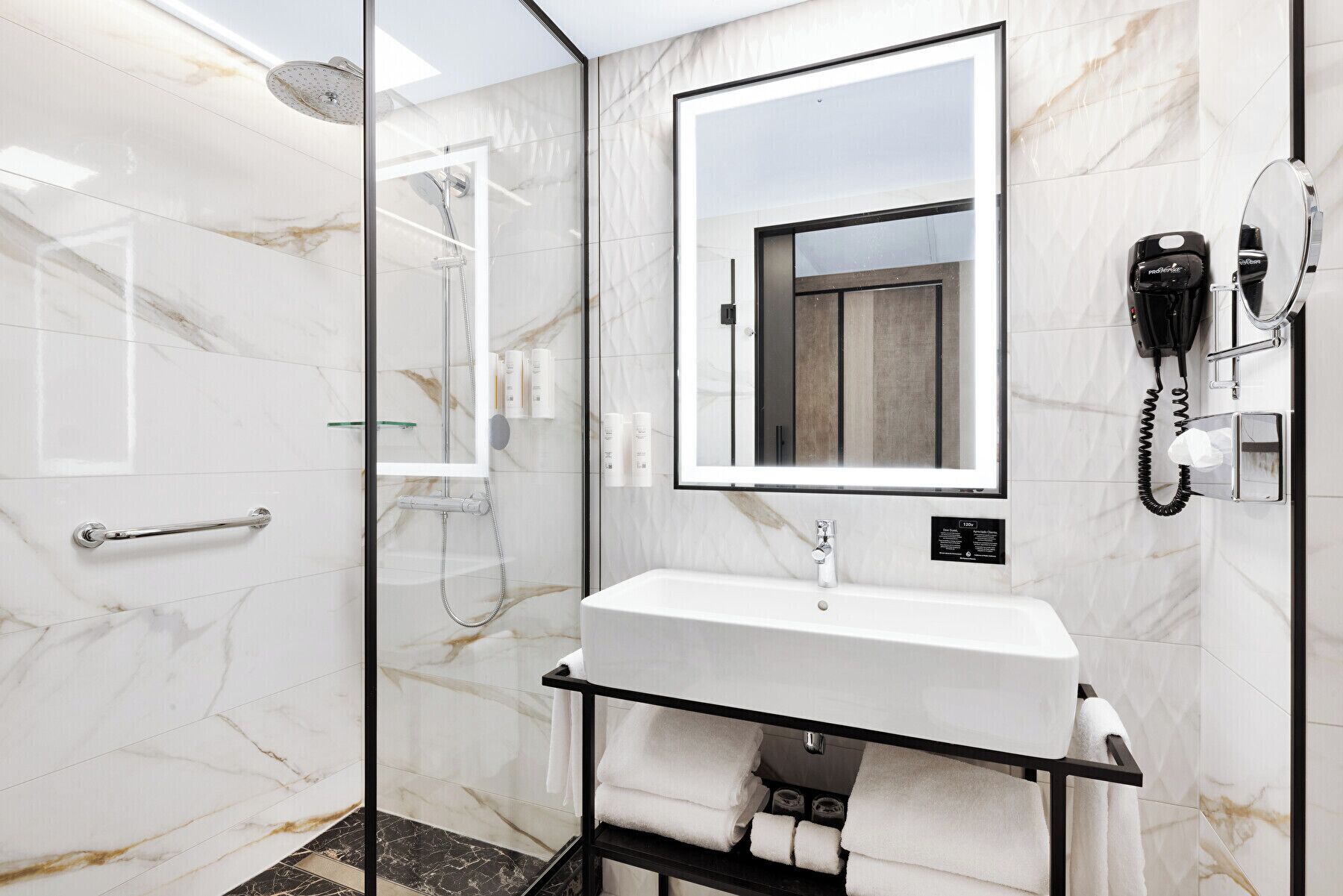 A modern bathroom with a glass-enclosed shower, a white sink with a mirror above it, and a telephone on the wall.