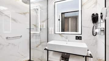 A modern bathroom with a glass-enclosed shower, a white sink with a mirror above it, and a telephone on the wall.