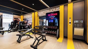 A gym with weightlifting equipment, a TV screen displaying 'The Kingdom', and motivational posters.