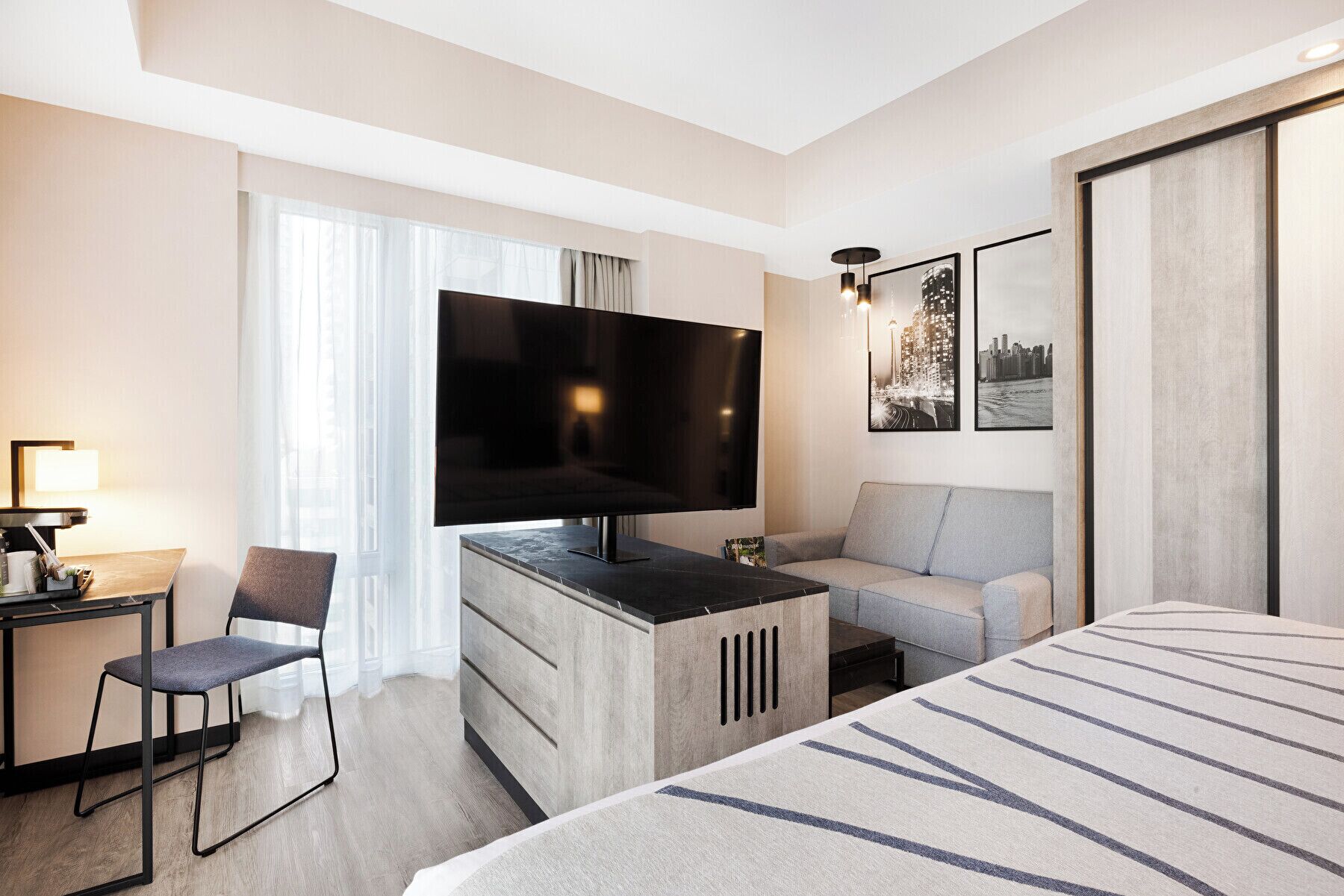 A hotel room with a large bed, a desk with a flat-screen TV, a sofa, and a chair.