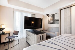 A hotel room with a large bed, a desk with a flat-screen TV, a sofa, and a chair.