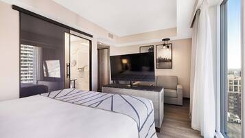 A modern hotel room with a large bed, a TV, a sofa, and a city view.