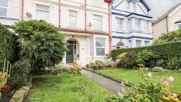 A two-story house with a front garden, a paved pathway, and a variety of plants and flowers.