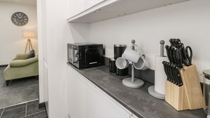 A modern kitchen with a microwave, coffee and tea containers, a knife block, and a clock on the wall.