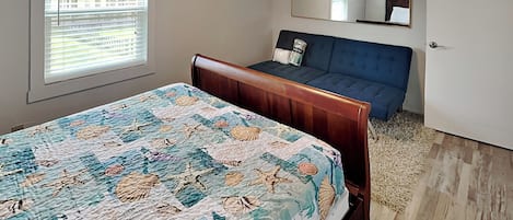 A bedroom with a bed, a blue sofa, a large window, and a mirror on the wall.