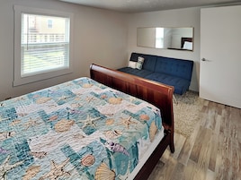 Un dormitorio con cama, un sofá azul, un ventanal grande y un espejo en la pared.