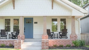 A single-story house with a blue front door, two front porches with chairs, and a brick foundation.