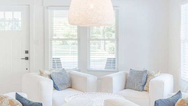 A bright, white room with two white sofas, a white coffee table, and a textured ceiling light.