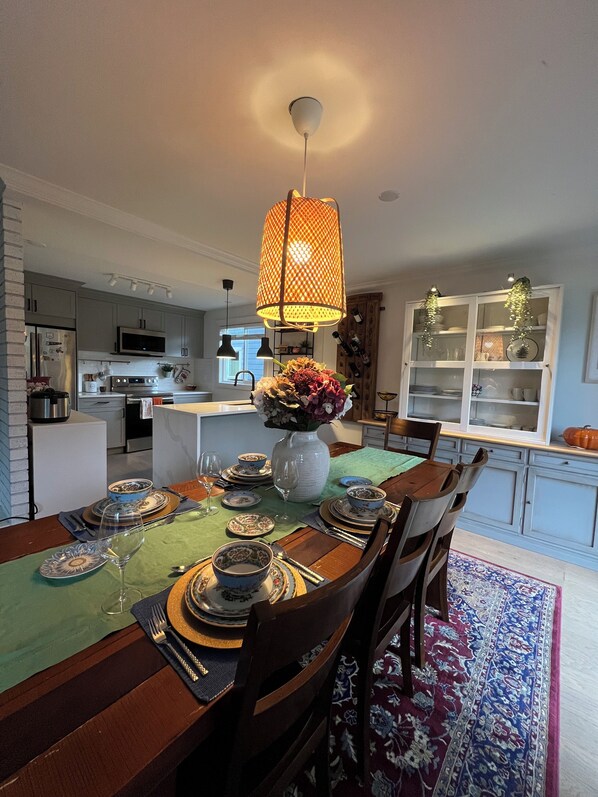 A dining area with a table set for four, a vase with flowers, and a hanging light fixture.