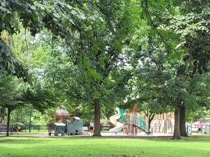 En park med legeudstyr, bænke og et stort træ.