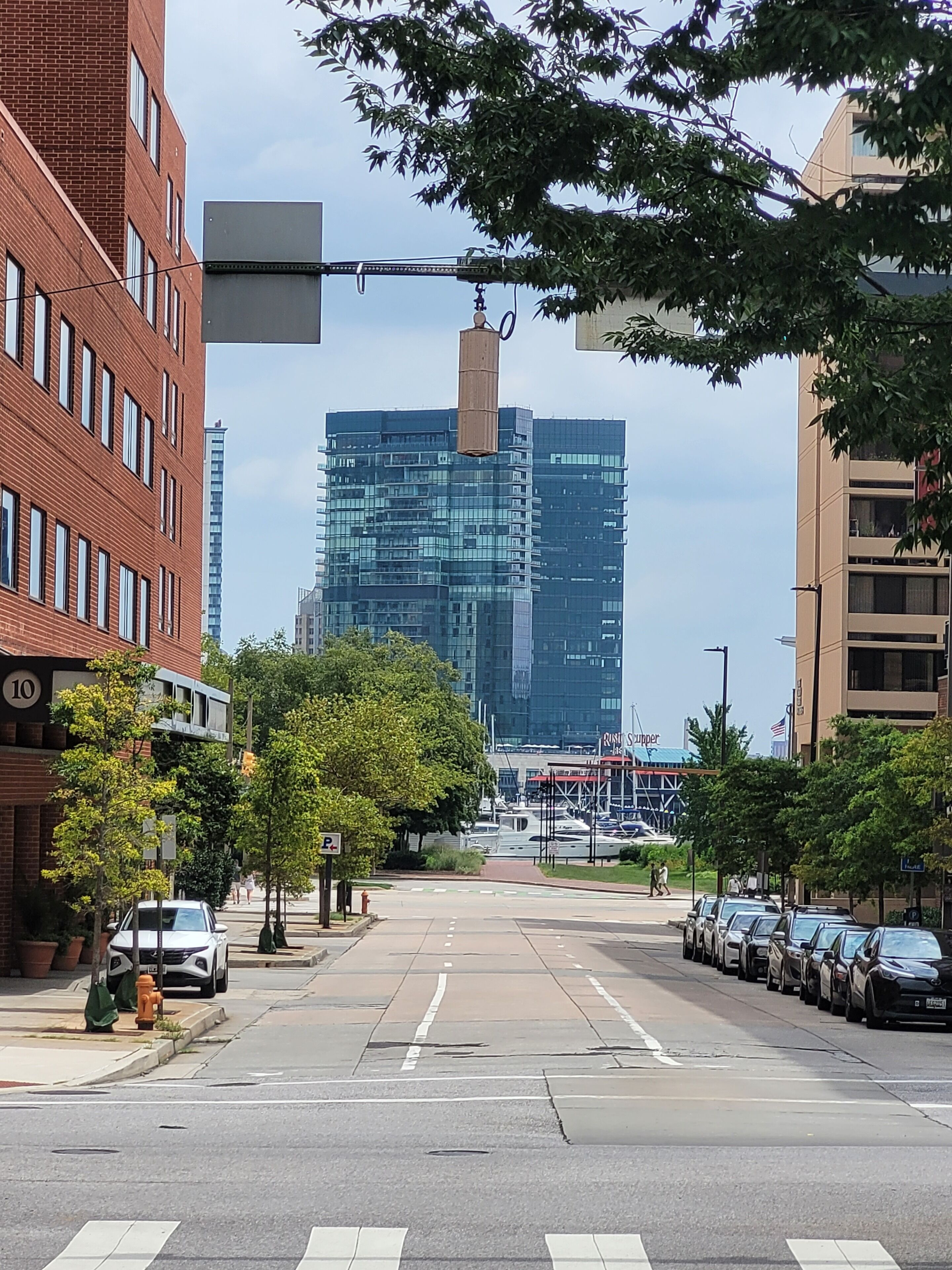 A street view with a row of parked cars, a pedestrian crossing, and a large building in the background.