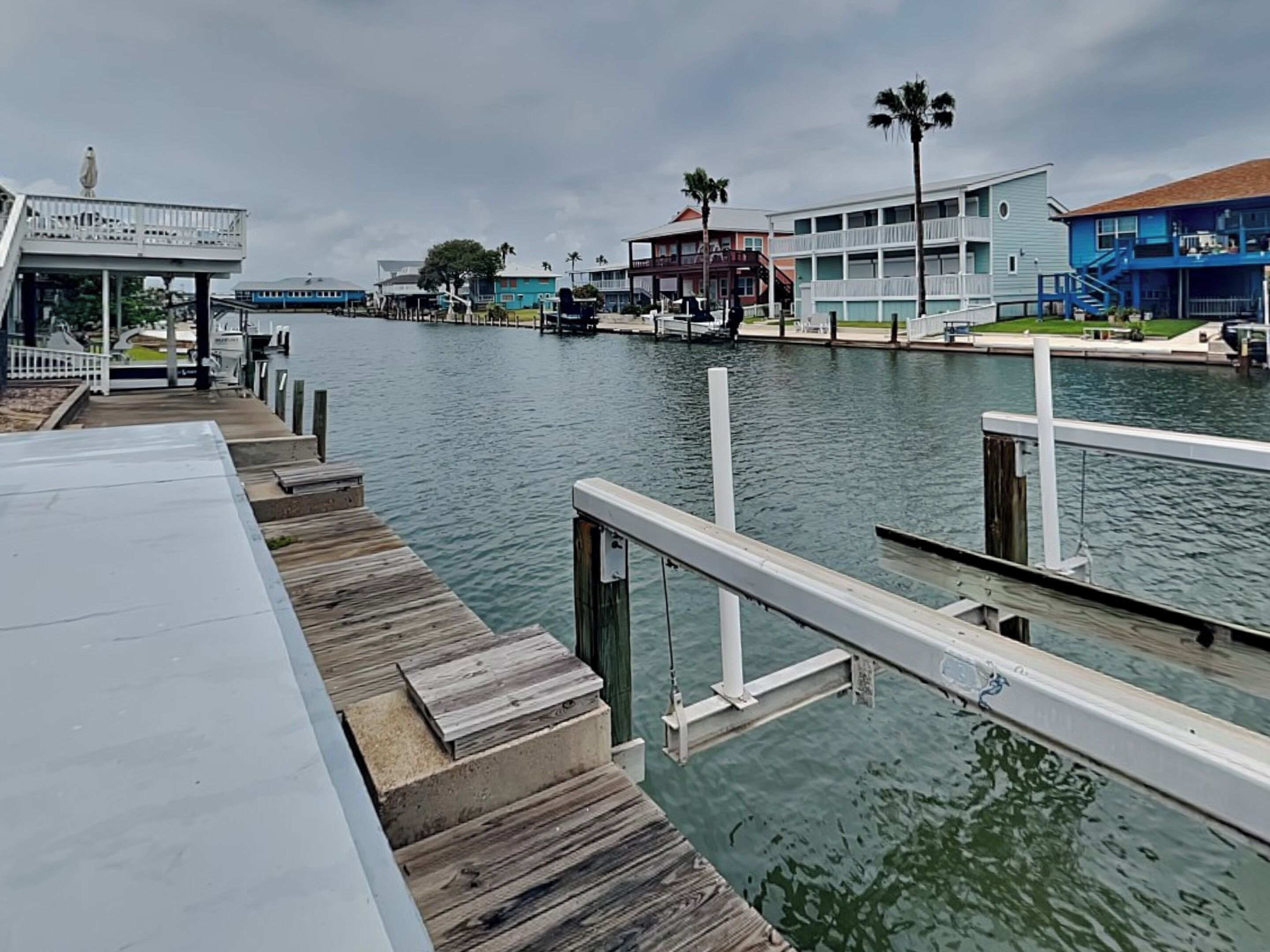 A waterfront dock with a wooden walkway leading to a building with a balcony and a statue.