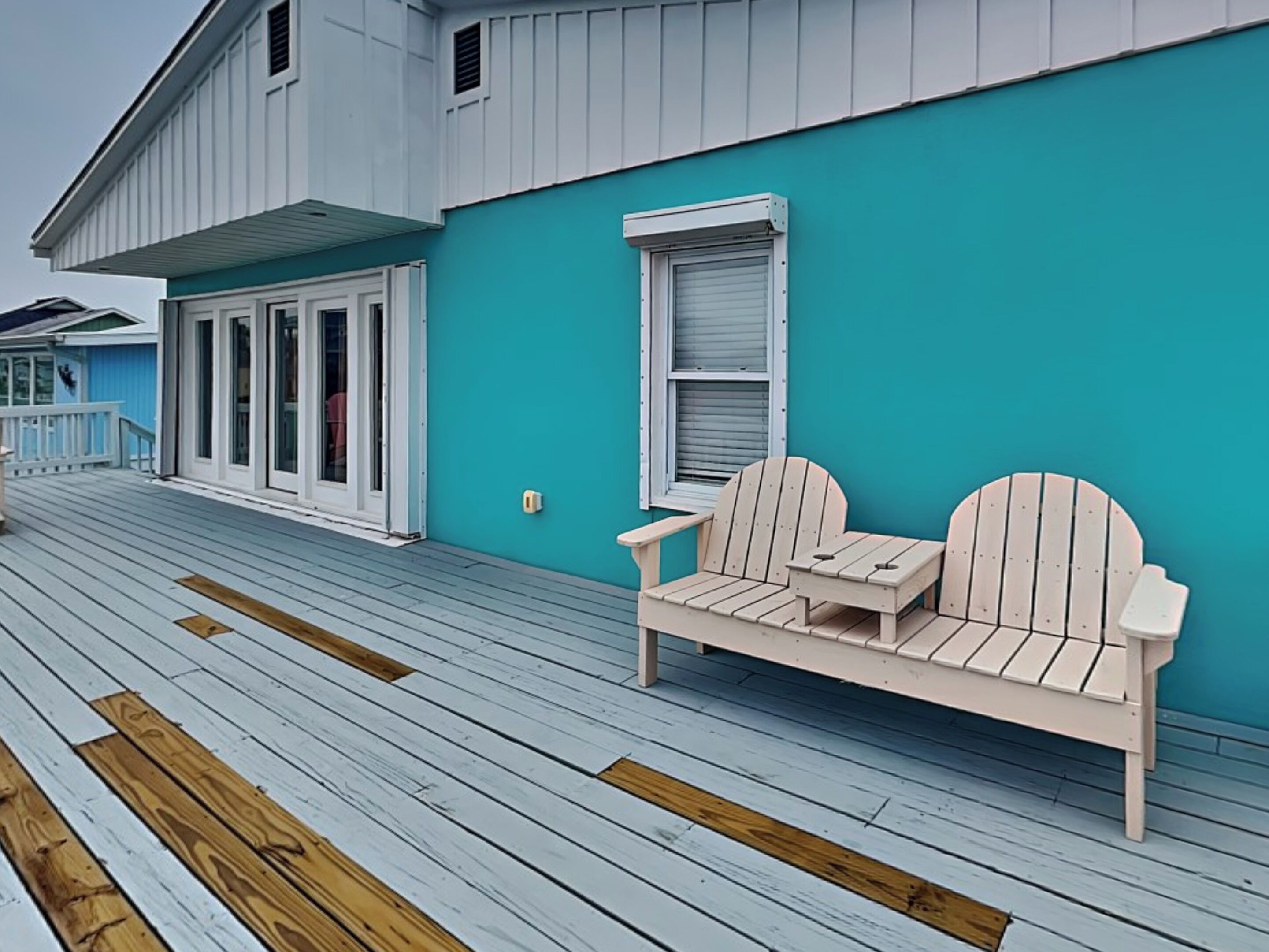 A wooden deck with a white Adirondack chair and a small table.