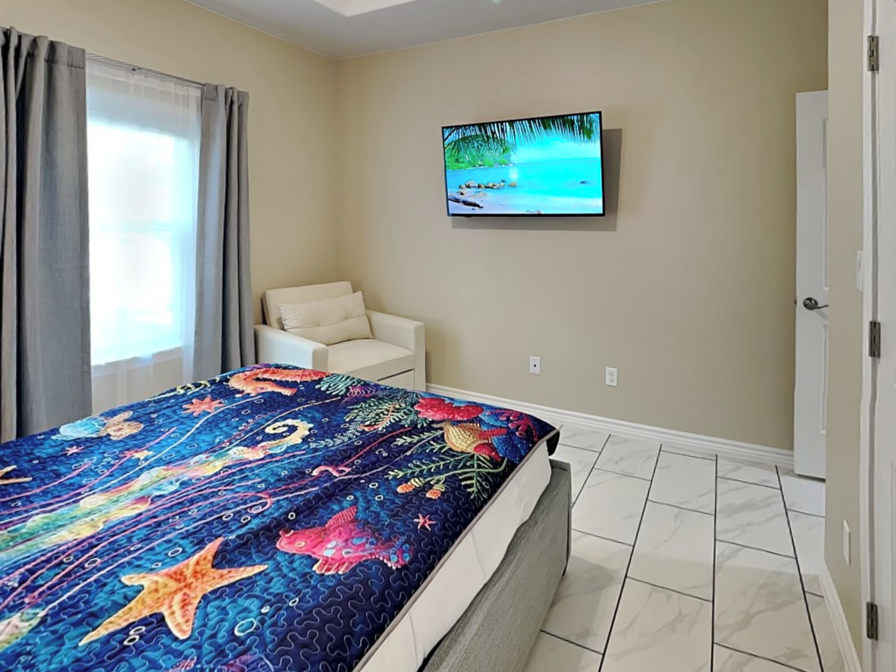 A bedroom with a bed, a television on the wall, a chair, and a door.