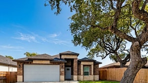 A two-story house with a garage, a front yard, and a large tree. - Ferryman's Landing by Miss Kitty’s (Aransas Pass)