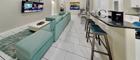 Ein modernes Wohnzimmer mit einem Ecksofa, einem an der Wand montierten Fernseher, einem Deckenventilator und einer Küchenzeile mit einem Barhocker.