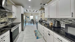A modern kitchen with white cabinets, stainless steel appliances, and a tiled floor. - Ferryman's Landing by Miss Kitty’s (Aransas Pass)