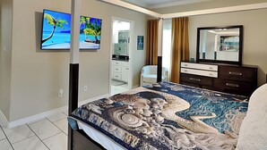 A bedroom with a large bed, a ceiling fan, a bathroom with a vanity, and a view of the ocean through the window. - Ferryman's Landing by Miss Kitty’s (Aransas Pass)