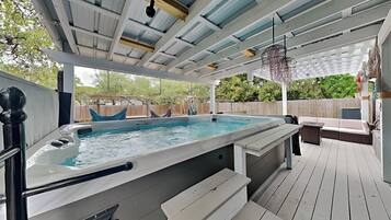 A hot tub with a wooden deck, a covered patio, and a hanging light fixture.