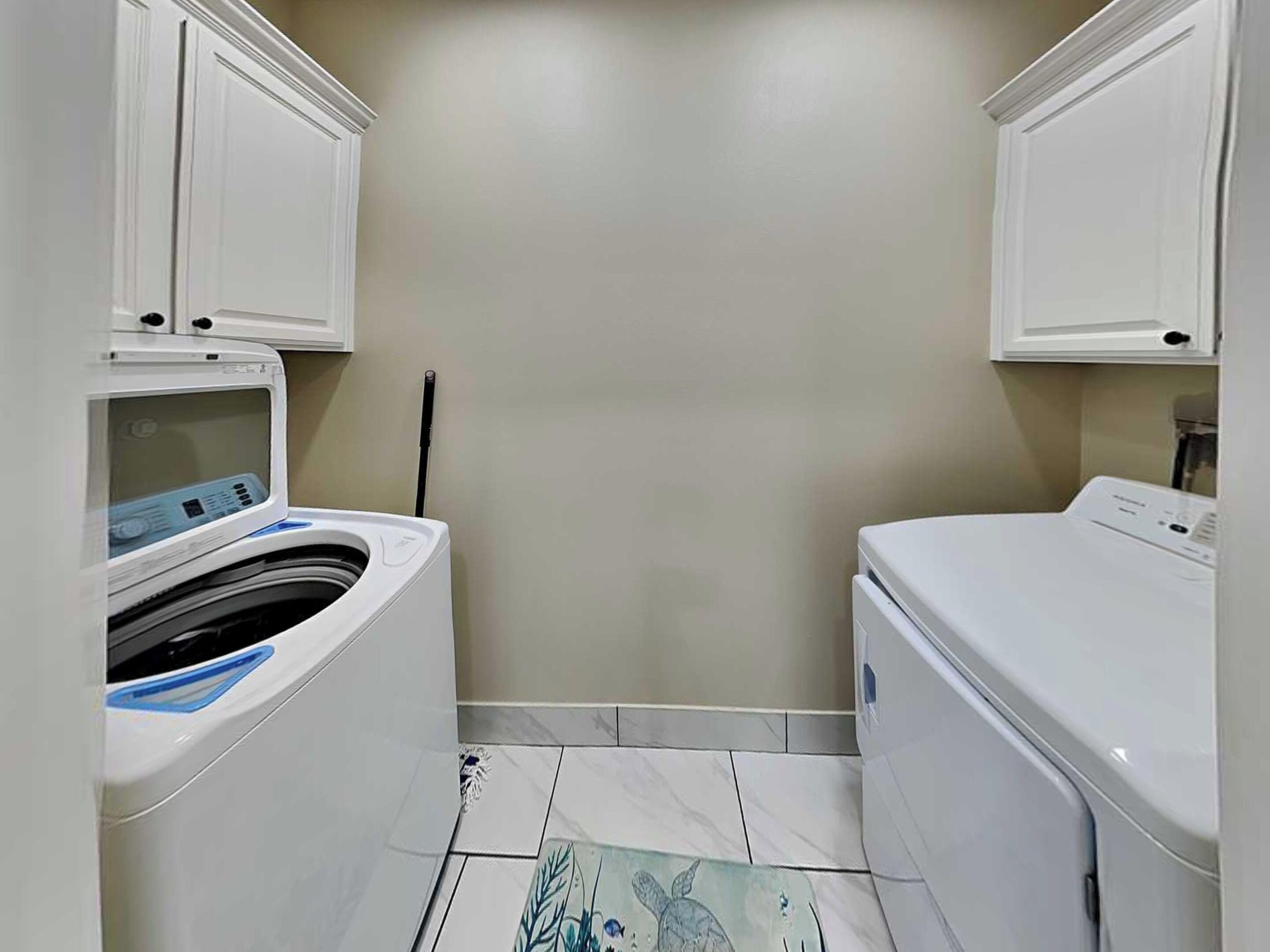 A laundry room with two washing machines, a tiled floor, and a wall-mounted cabinet.