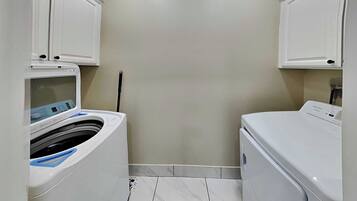 A laundry room with two washing machines, a tiled floor, and a wall-mounted cabinet.