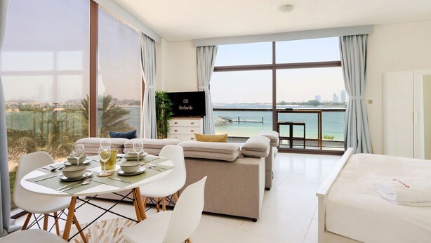 Habitació d'hotel moderna amb zona de menjador, sofà, televisió i balcó amb vista al mar.