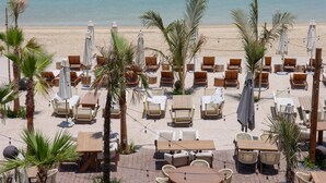 Un cafè a la vora de la platja amb caires i taules de fusta, ombrel·les i palmeres.