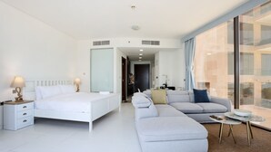 Una habitació d'hotel moderna amb un llit, un sofà, una taula petita i vista a la ciutat a través de grans finestres.