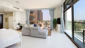 Habitació d'hotel moderna amb un llit gran, un sofà, zona de dinar i un balcó amb vista a la ciutat.
