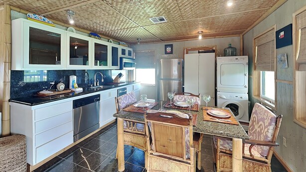 Une cuisine compacte dotée d’appareils électroménagers modernes, un coin repas avec des chaises en osier et un sol carrelé.