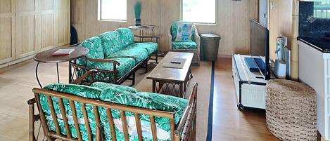 A room with a wooden floor, a sofa, a chair, a small table, a trash bin, and a pool table.