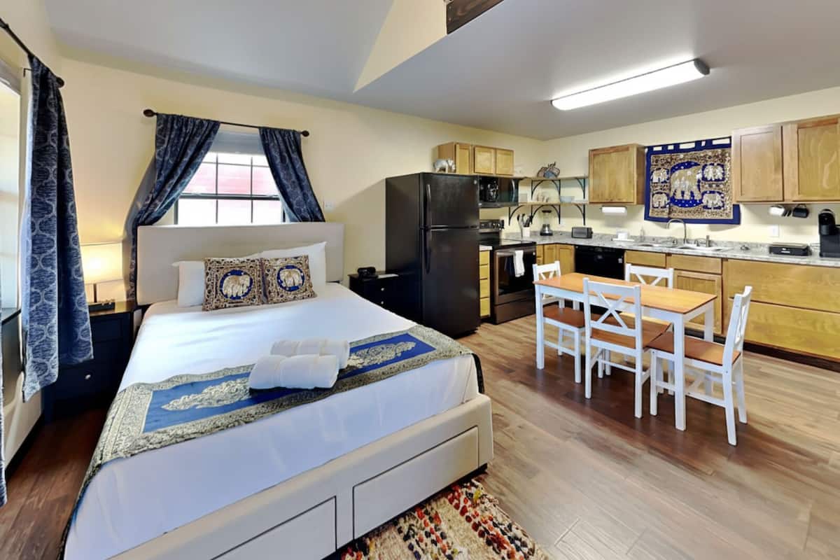 A bedroom with a bed, a small desk, and a kitchenette.