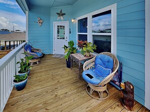 A covered porch with two wicker chairs, a small table, and potted plants. - Kat's Place by Miss Kitty’s (Rockport)